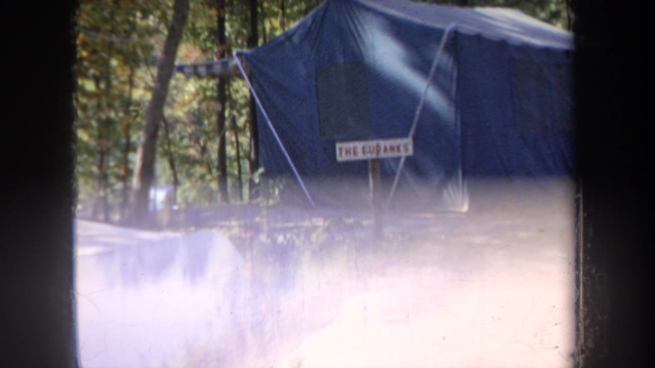 Blue canvas tent and campsite sign partly washed by bright exposure flare.