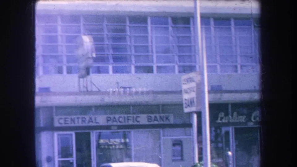 1969 Hawaii commercial facade with Central Pacific Bank signage, upper louvered windows, a foreground street sign, and adjacent retail sign.