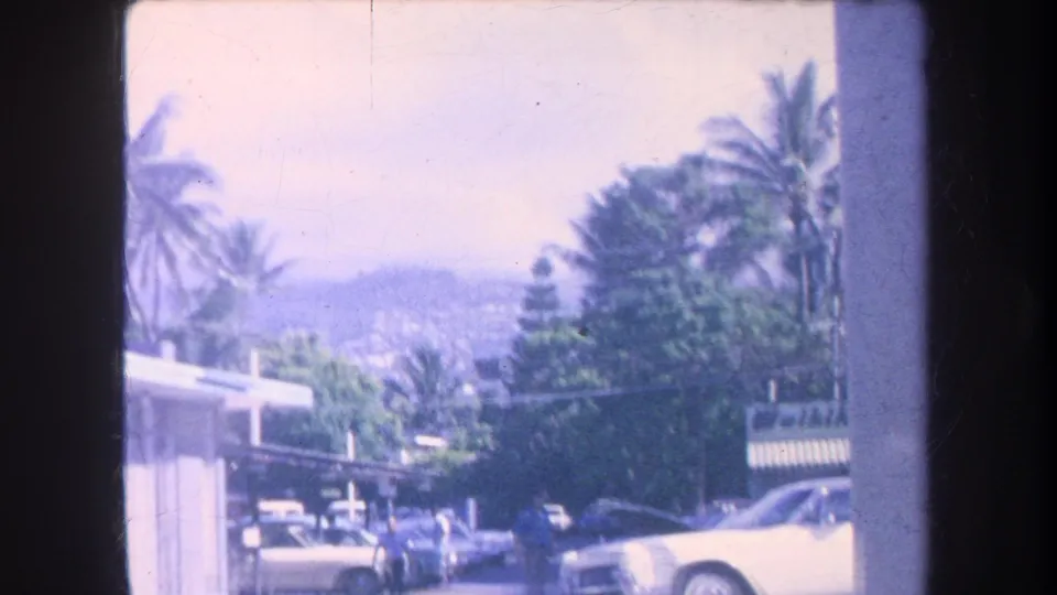 1969 Hawaii street view showing palm trees, several cars, and a bus or trolley moving through a beach-town corridor.