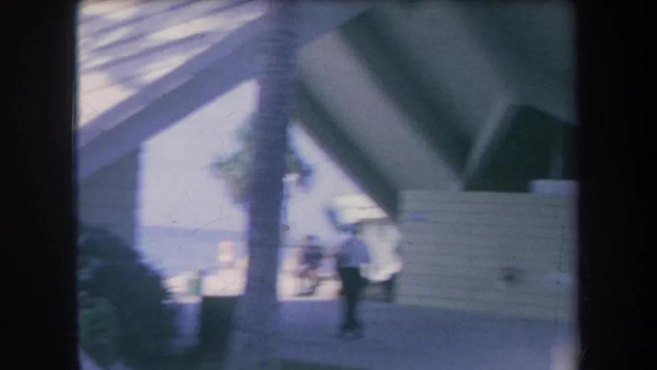 1969 Hawaii 8mm frame showing a covered building walkway with a distant person moving near the entrance area.