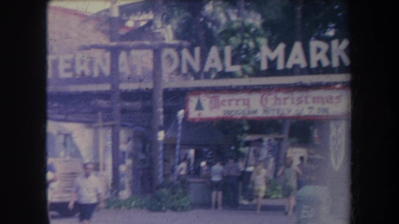 Pedestrians walking outside the International Market beneath a Merry Christmas sign.