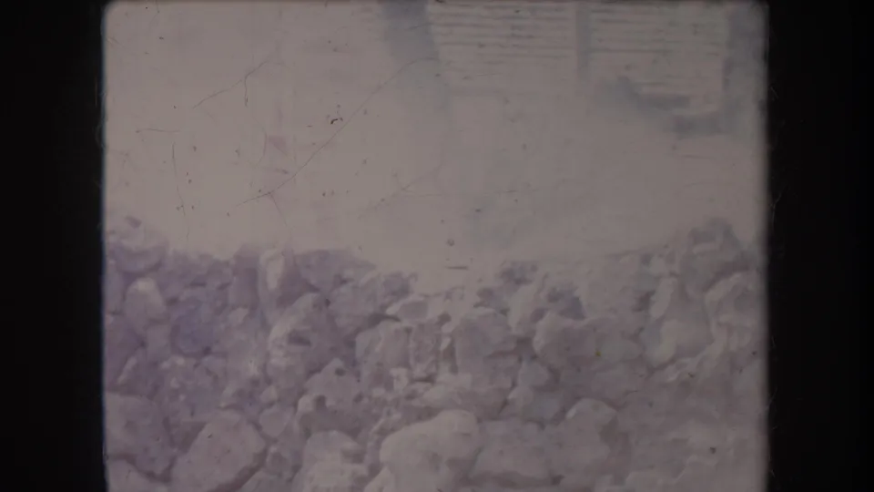 Faded 1969 Hawaii home-movie frame with rocks or a stone wall and a hazy outdoor background, with no clear faces visible.