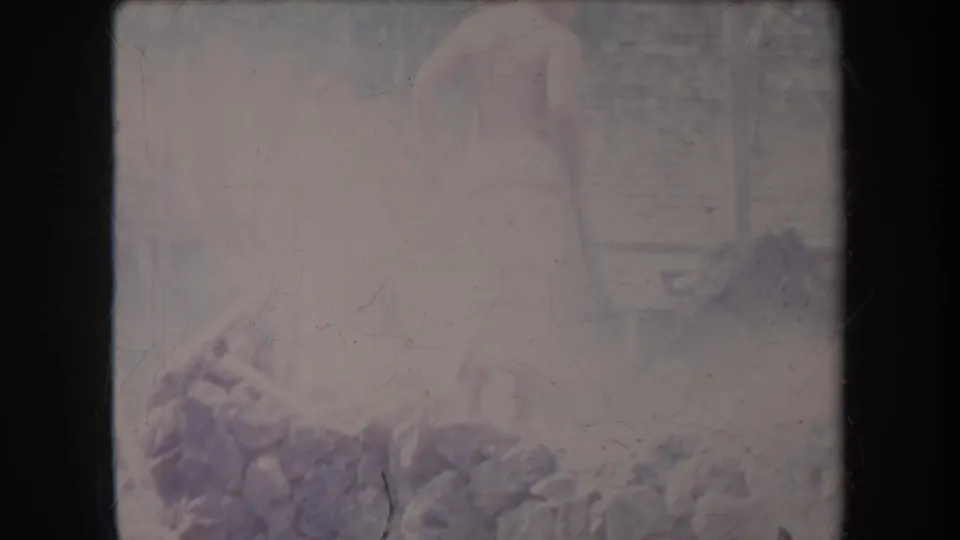 A shirtless figure appears partly obscured beside rocks or a stone wall in faded 1969 Hawaii 8mm footage.