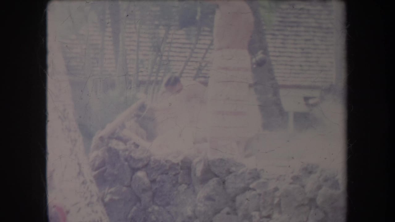 Person in a light skirt or wrap standing beside rocks and wood outdoors.