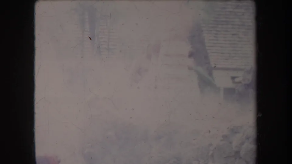 Very faded 1969 Hawaii home-movie frame showing a partial figure near rocks, wood, and a slatted fence outdoors.