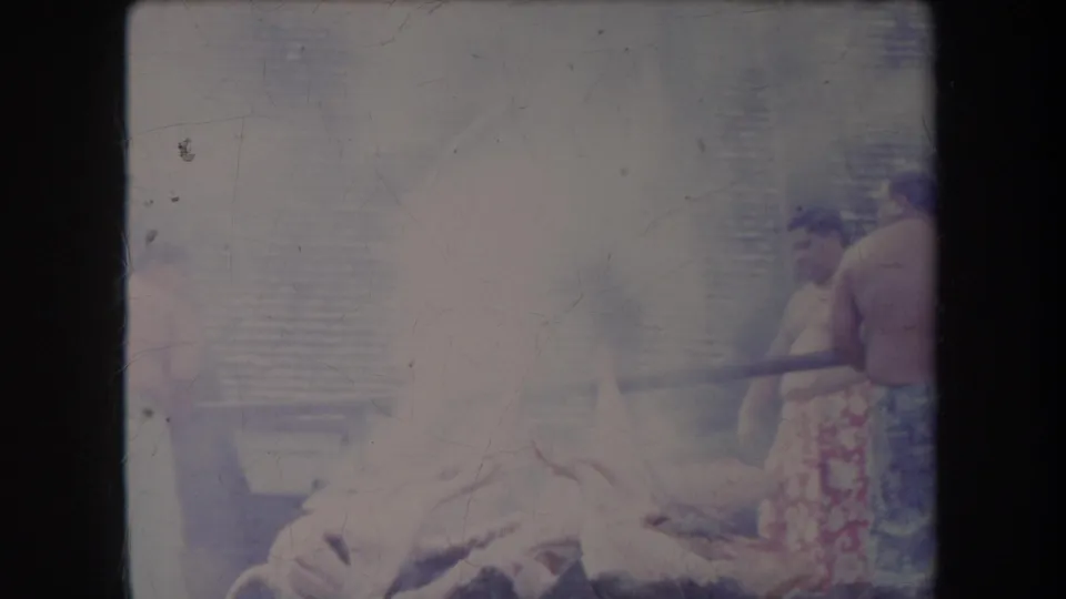 Faded 1969 Hawaii 8mm frame showing men near a smoky pig roasting pit, partly obscured by exposure and haze.