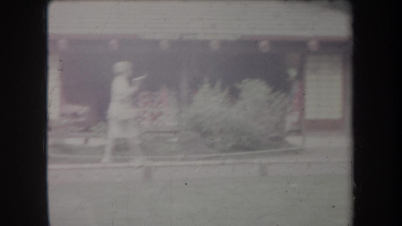 A person stands near a landscaped bed in front of a low building.