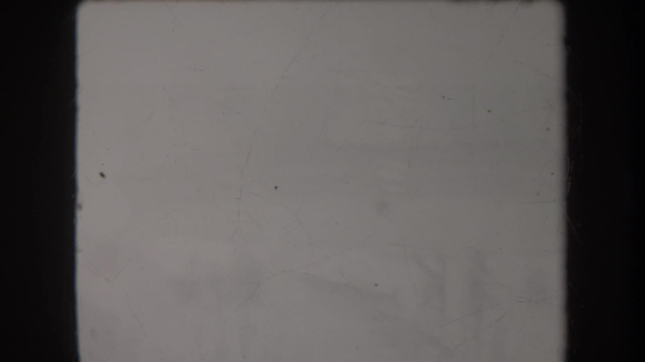 A mostly blank 8mm frame with scratches, muted gray exposure, and dark vertical film borders at the start of the clip.