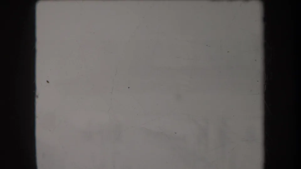 A mostly blank 8mm frame with scratches, muted gray exposure, and dark vertical film borders at the start of the clip.