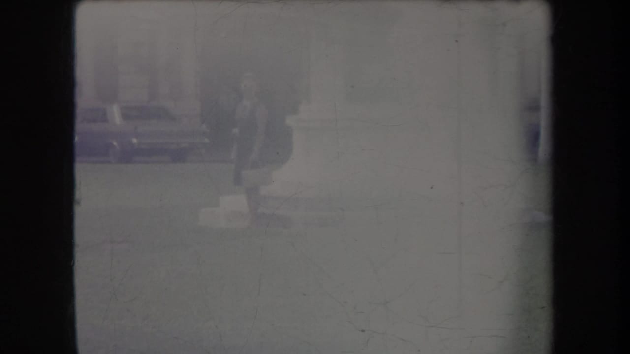 Faded Hawaii home-movie frame with a faint parked car, pavement, and a partially visible person near the top edge.