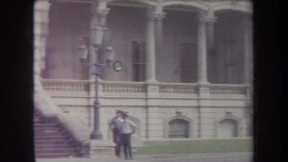 1969 Hawaii 8mm frame of the lower facade, exterior stairs, street lamps and two visitors near the building.