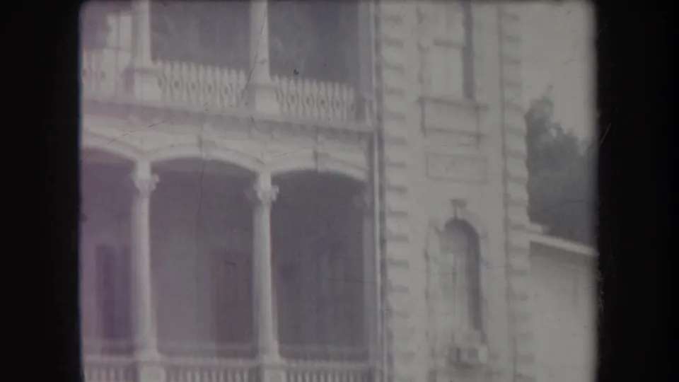 1969 Hawaii view of a columned lower balcony, arched window and pale stone exterior in soft 8mm footage.