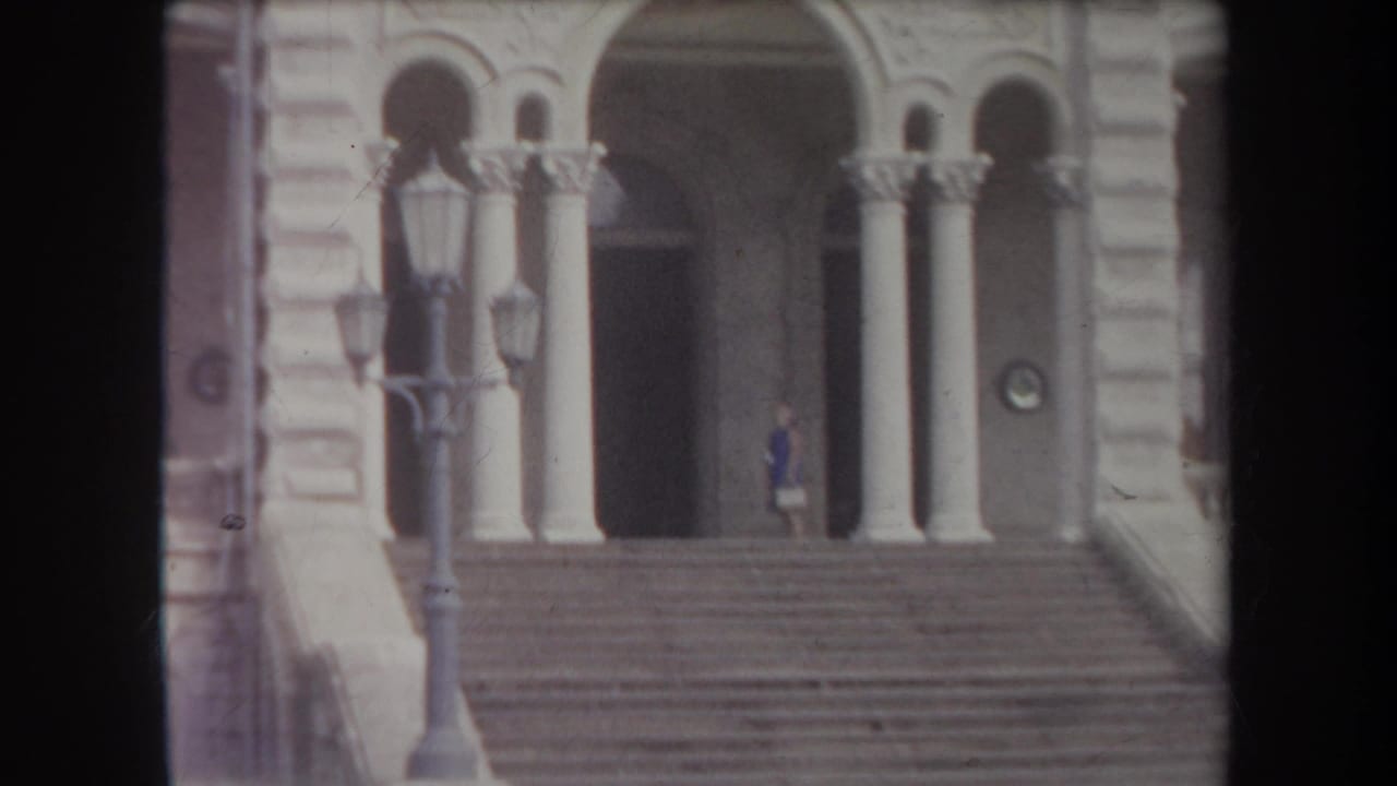 1969 Hawaii frame showing a columned stone entrance, broad steps, lampposts, and a person standing near the doorway.