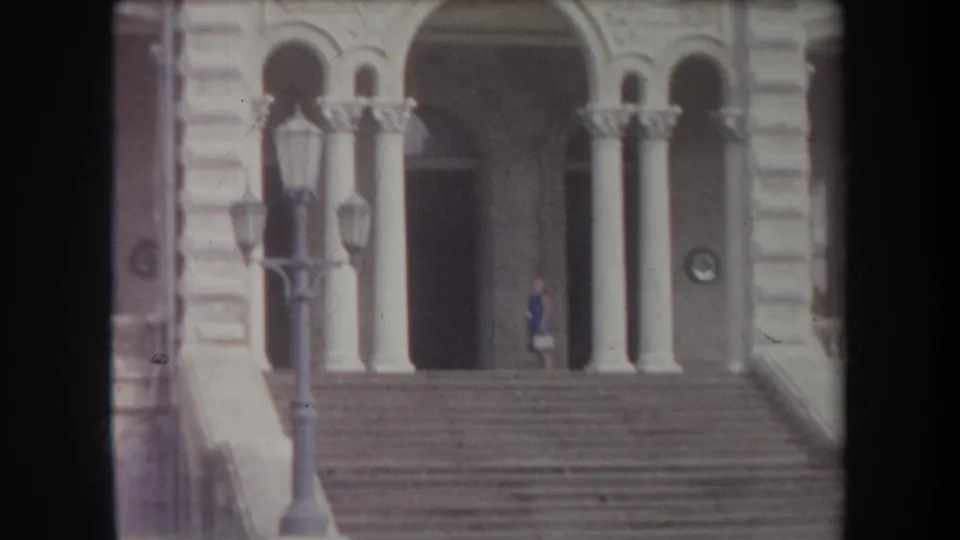 1969 Hawaii frame showing a columned stone entrance, broad steps, lampposts, and a person standing near the doorway.