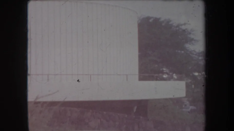 1969 Hawaii 8mm frame with a pale wall or structure, railing, trees, and a low stone base in soft exposure.