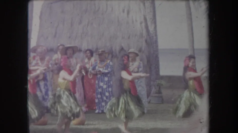 Hawaii 1969 frame with hula dancers performing in the foreground and tourists in patterned clothing watching behind them.