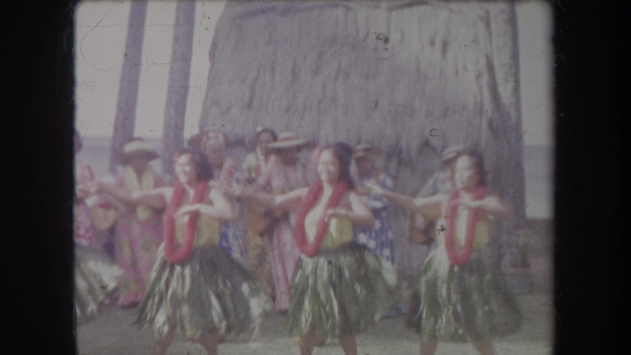 Hula dancers extend their arms while performers stand behind them.