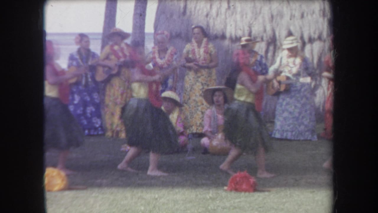 Two hula dancers move in front of musicians wearing floral clothing.