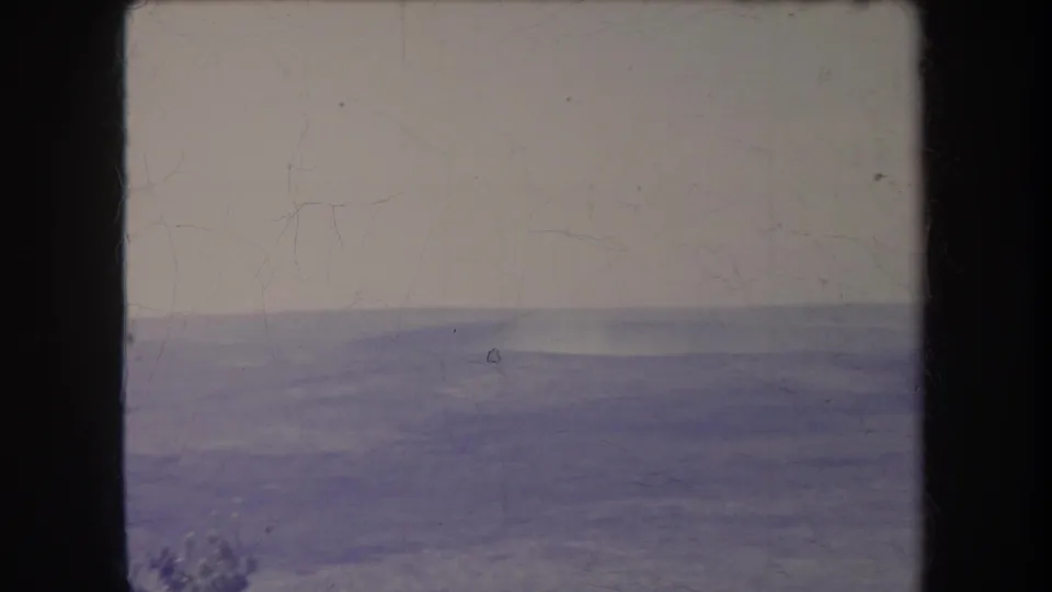 Static 8mm view of soft blue-purple ridges beneath a pale sky, with rounded frame edges and visible surface wear.