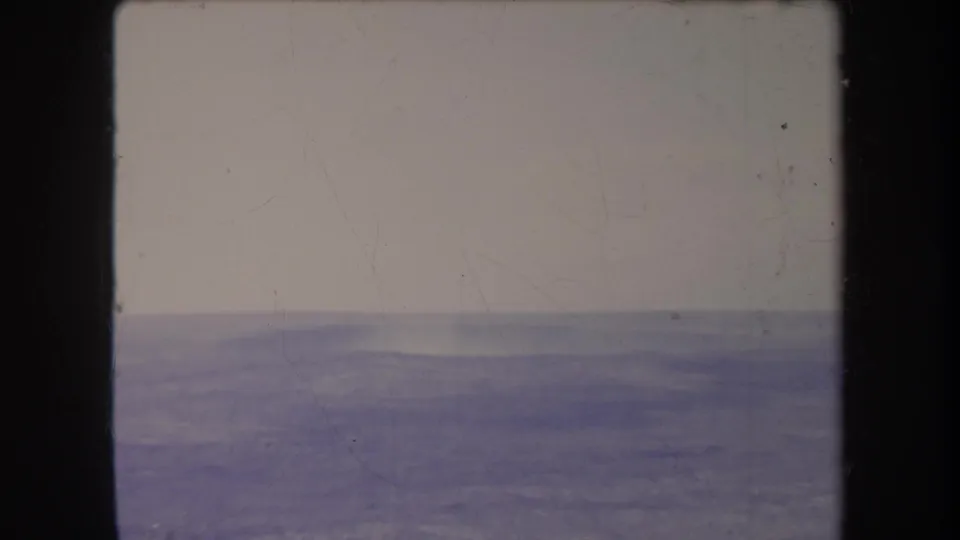 Aged 8mm frame showing a low, hazy ridge across the bottom portion of the picture beneath a washed pale sky.
