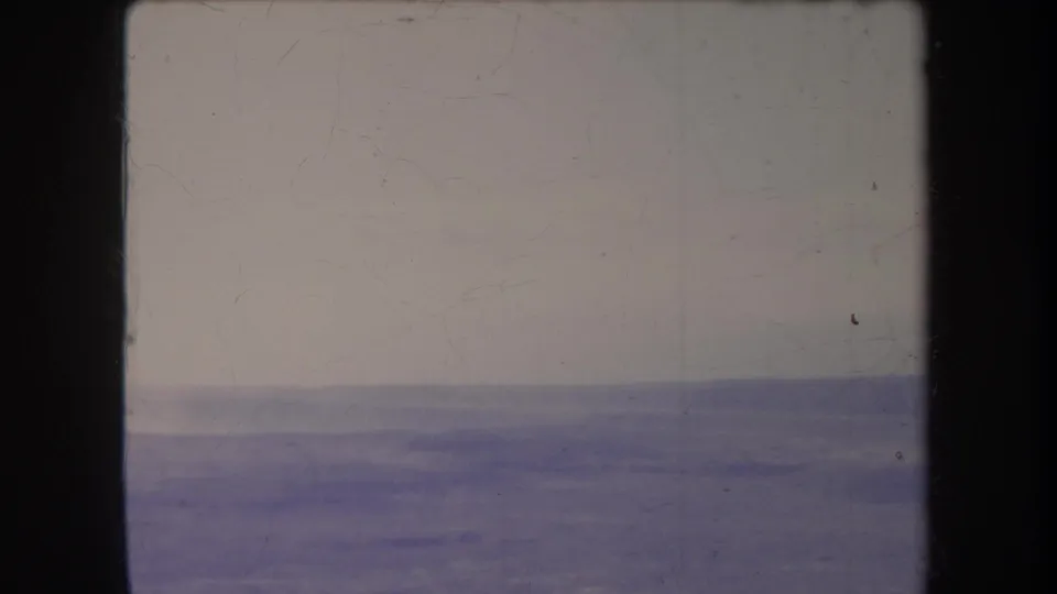 Faded 1969 8mm landscape frame with distant horizontal ridges, pale sky, dark borders, and visible dust marks.