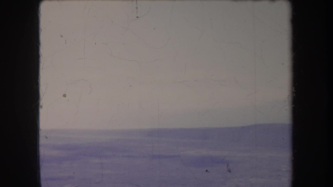1969 Hawaii 8mm frame showing a distant hazy ridge beneath a pale sky, with visible gate edges and film wear.