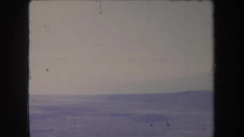 1969 Hawaii 8mm frame showing a distant hazy ridge beneath a pale sky, with visible gate edges and film wear.