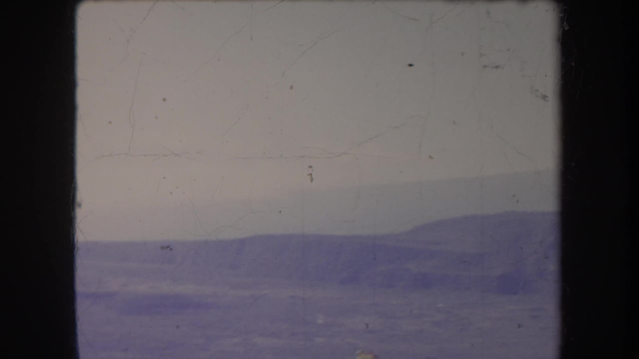 Distant hills and pale sky seen through faded, scratched film.