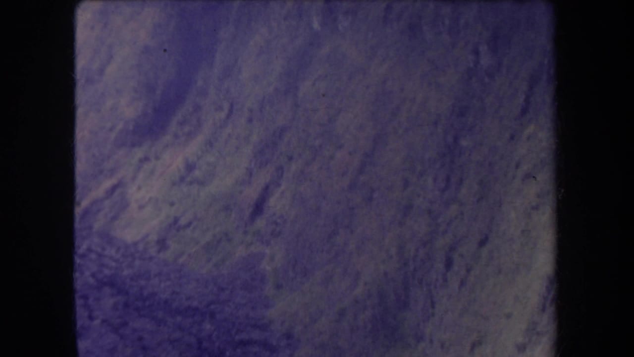 1969 Hawaii 8mm frame showing a rocky ravine slope with dirt textures, brush, and a purple aged-film cast.