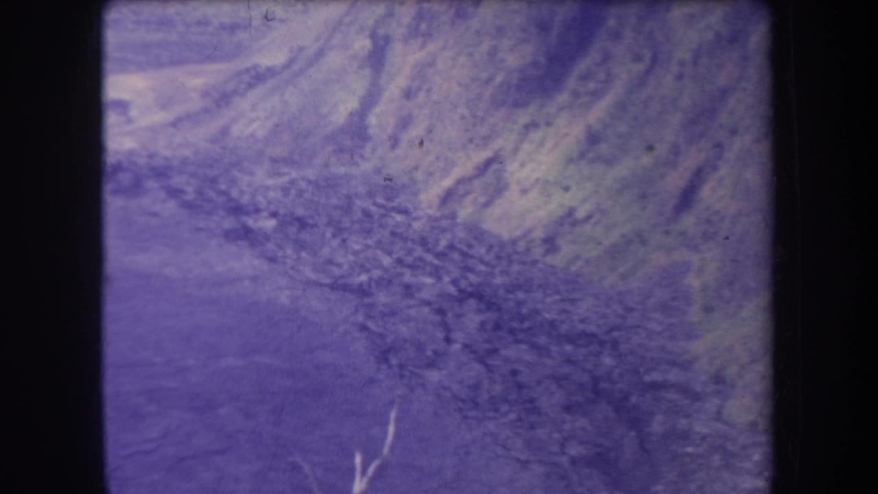 Steep ravine view with rocky ground, pale slopes, and film wear.