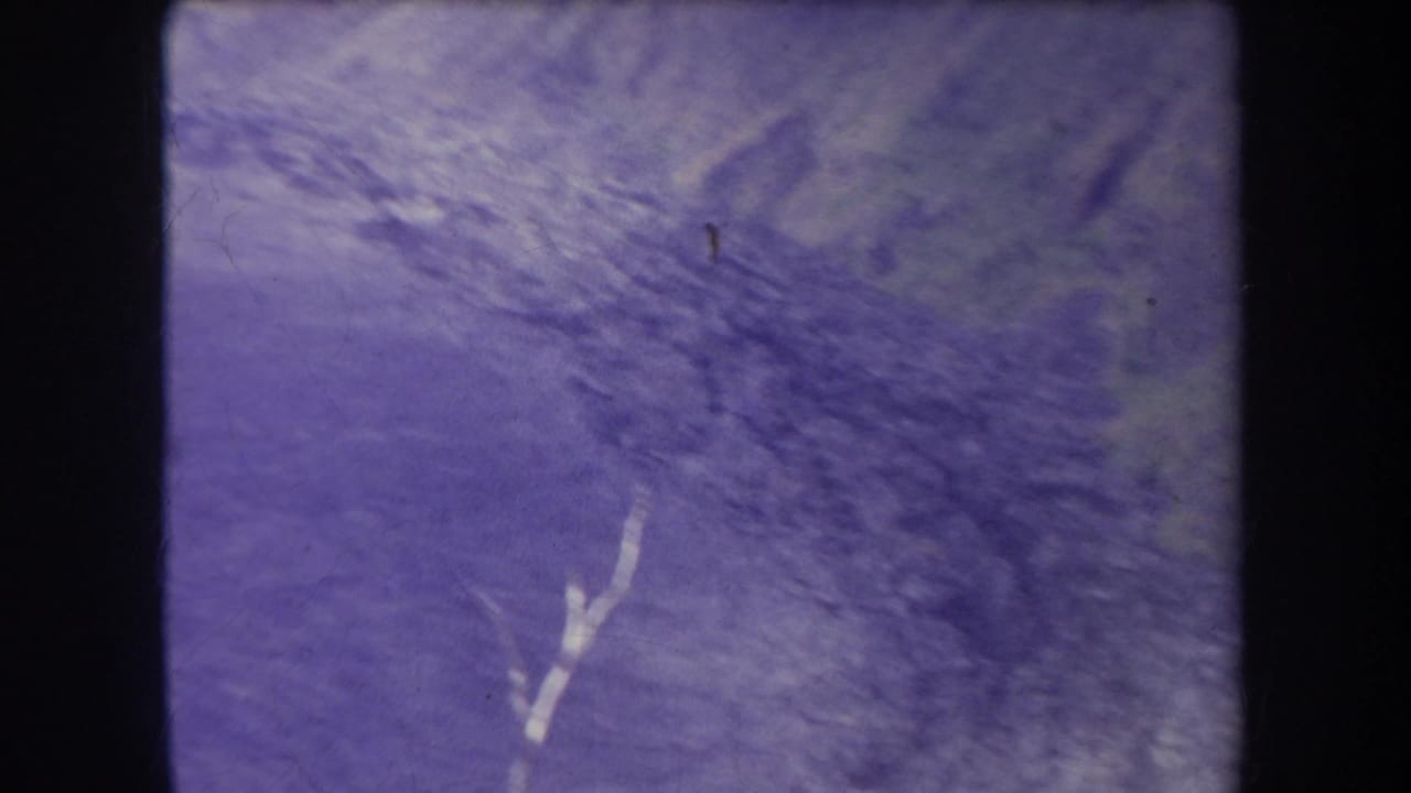 Faded 1969 Hawaii 8mm frame showing a hazy mountain surface or ridge area with scratches, grain, and blue-purple color shift.