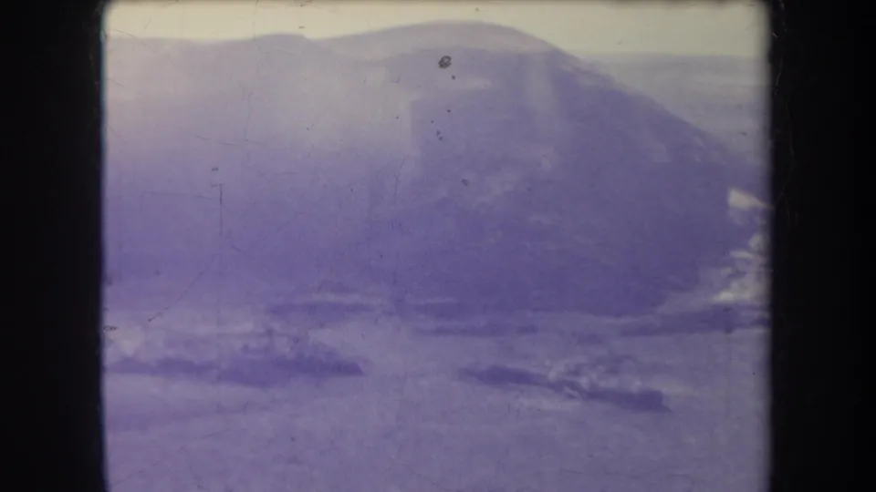 1969 Hawaii 8mm frame showing a broad hazy ridge and shimmering lower terrain, tinted by aged blue-purple film color.