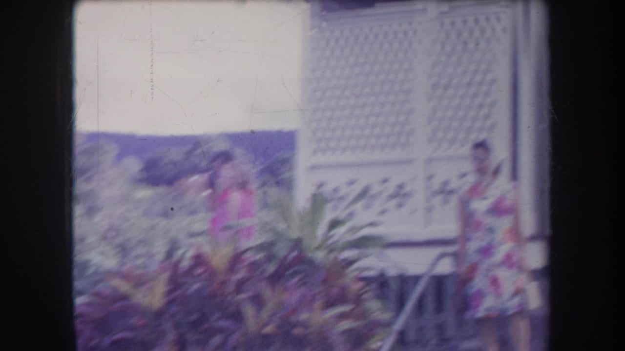 Woman in a pink and white floral dress near a white bungalow with lattice siding.