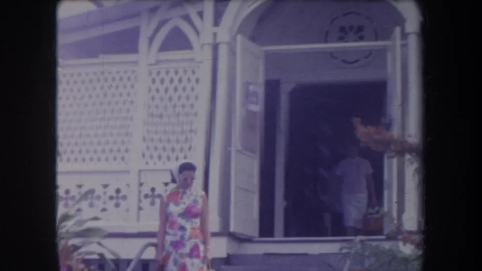 1969 Hawaii frame showing a woman in a floral dress near an arched bungalow entrance with lattice siding.