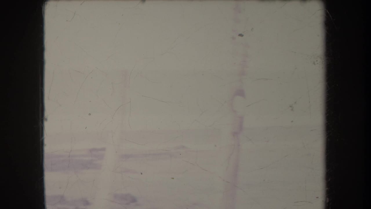 1969 Hawaii home-movie frame showing a washed-out beach horizon, pale surf line, and distant vertical structure through film fading.