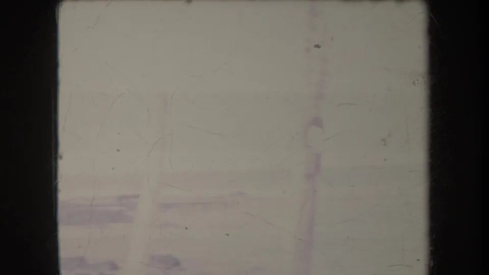 1969 Hawaii home-movie frame showing a washed-out beach horizon, pale surf line, and distant vertical structure through film fading.