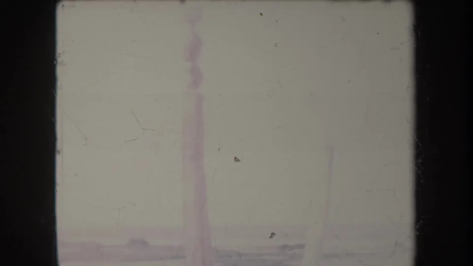 1969 Hawaii shoreline frame with a faint surf line and distant vertical structure, softened by color fading and dust.
