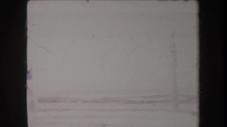 Faded 1969 Hawaii beach frame showing a low shoreline, pale sky, and indistinct vertical forms near the frame edge.