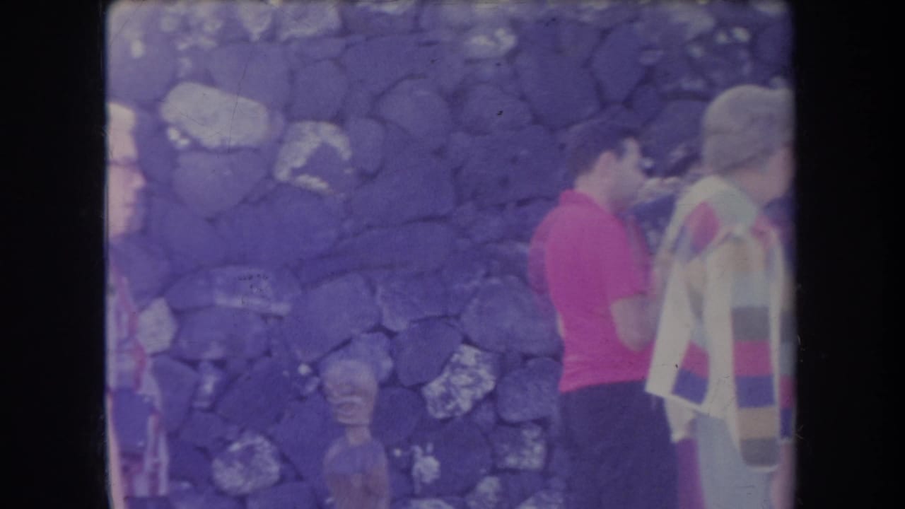 A red-shirted visitor and other tourists stand by a stone wall.