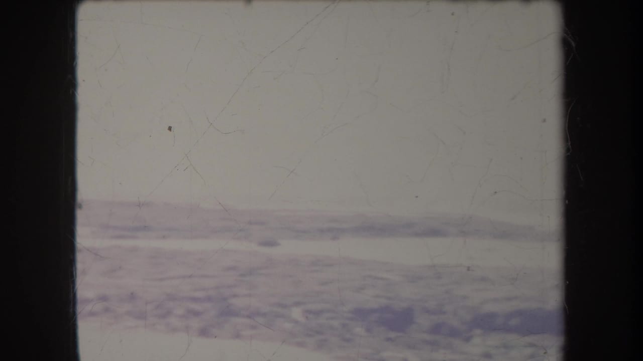 1969 Hawaii 8mm frame showing a pale beach and waterline with soft focus, scratches, and dark film gate borders.