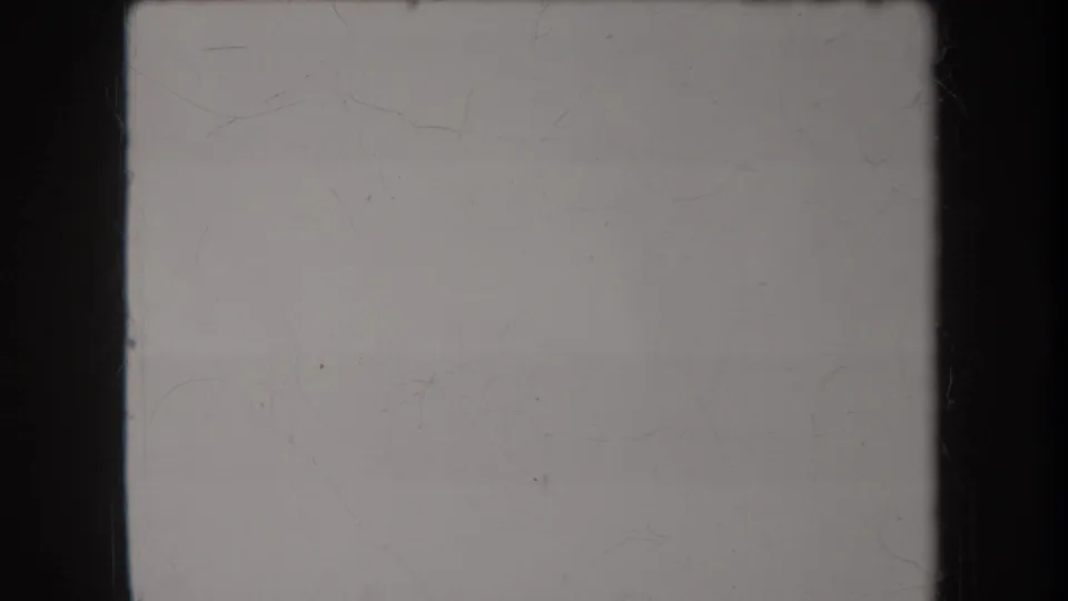 Pale overexposed 8mm frame from the Hawaii clip, with scratches, dust, and black film edges visible.