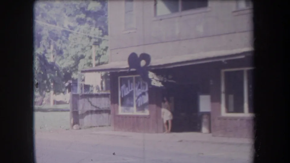 1969 Hawaii street view of a small storefront with awning, sign shape, sidewalk, posted notice, and a person near the door.