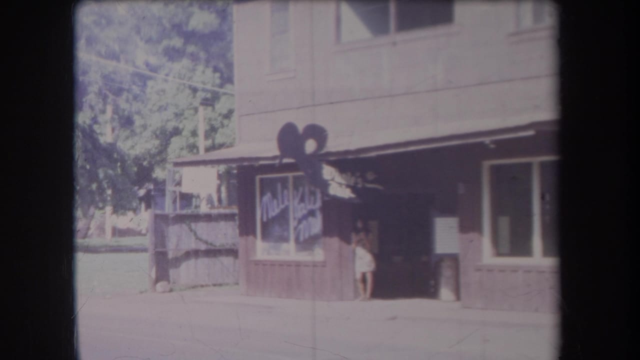 Storefront and awning with a woman at the entrance and trees visible at left.