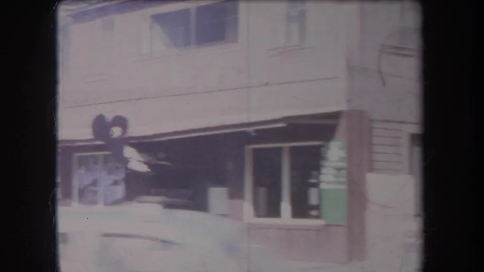 Handheld 1969 Hawaii frame passing a small commercial facade with awning, sign, doorway, windows, and street-side details.