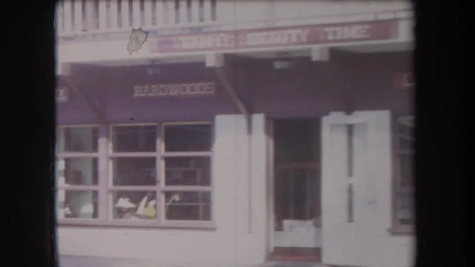 1969 Hawaii street view of a shopfront with dark awnings, large windows, a doorway, and visible business names on the facade.