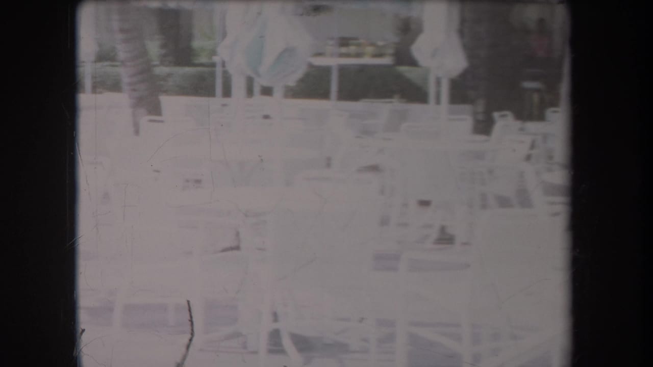 Overexposed patio area with white chairs, umbrellas, tables, and a hedge line.