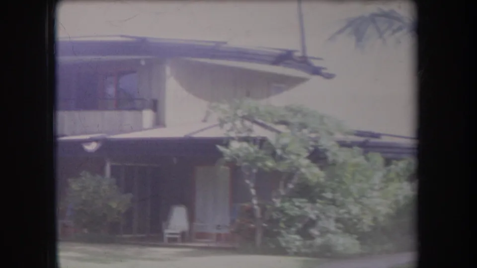 1969 Hawaii home-movie view of a mid-century house exterior behind tropical landscaping.