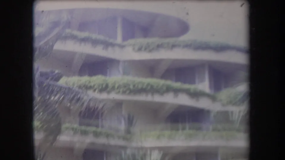 1969 Hawaii 8mm view of a multi-story lodging or condominium facade with planted curved balconies during windy weather.