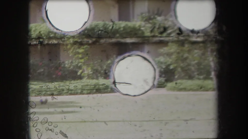1969 Hawaii 8mm frame with circular overexposed marks across a planted building exterior, lawn, and soft storm-weather scene.