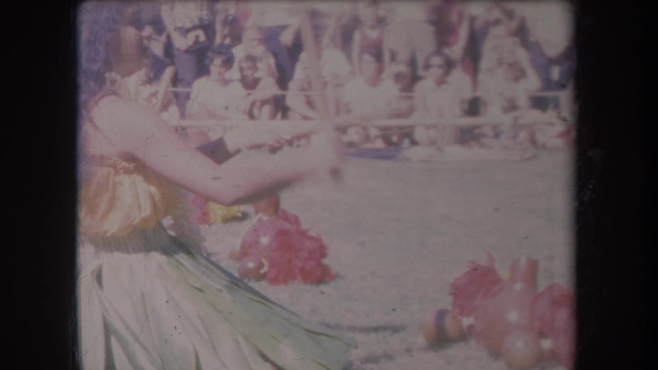 1969 Hawaii 8mm frame showing two women in hula-style costumes dancing before spectators behind a barrier.